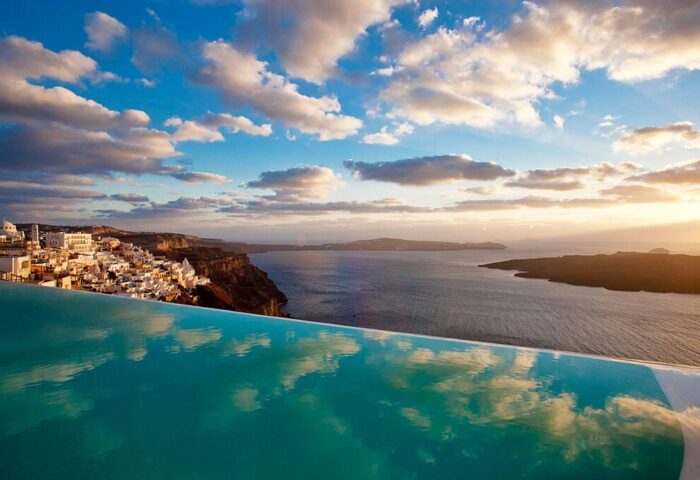 Cosmopolitan Suites, a gay-friendly hotel. Infinity pool overlooking Santorini's caldera, Aegean Sea, and whitewashed buildings on the cliff.