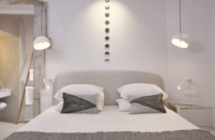 Cosmopolitan Suites gay-friendly hotel bedroom. Minimalist design, white linens, decorative pillows, and lunar phase wall art. Stylish gay travel.