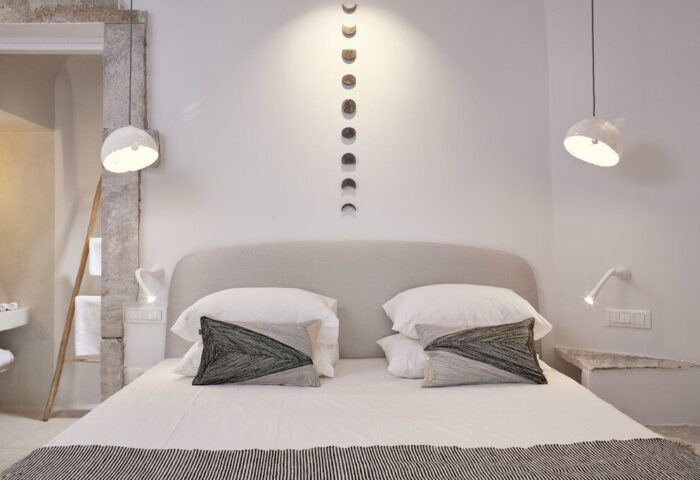 Cosmopolitan Suites gay-friendly hotel bedroom. Minimalist design, white linens, decorative pillows, and lunar phase wall art. Stylish gay travel.