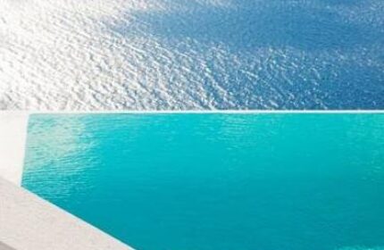 Infinity pool overlooking the sea at Cosmopolitan Suites, a gay-friendly hotel. Turquoise water blends with the ocean horizon. Serene travel destination.