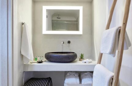 Cosmopolitan Suites gay-friendly hotel bathroom. Features a stone sink, illuminated mirror, and ladder towel rack. Luxury travel for gay men.