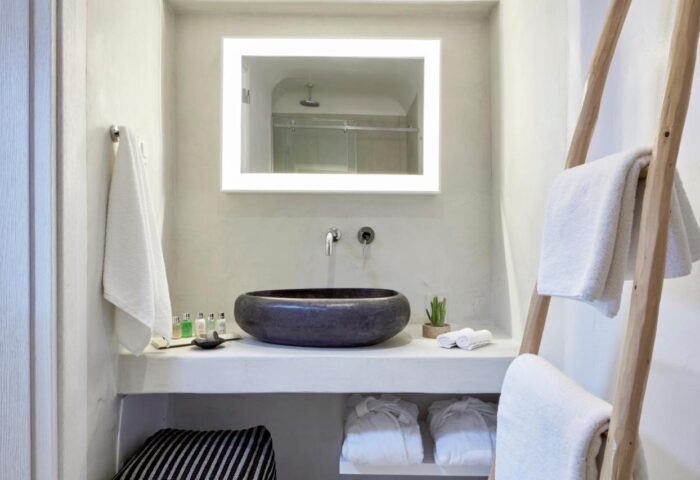 Cosmopolitan Suites gay-friendly hotel bathroom. Features a stone sink, illuminated mirror, and ladder towel rack. Luxury travel for gay men.