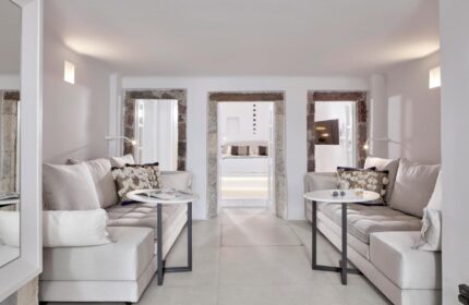 Cosmopolitan Suites gay-friendly hotel interior. White sofas, round tables, and stone doorways leading to a bedroom. Luxury travel vibe.