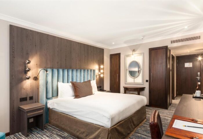 Courthouse Hotel bedroom: A gay-friendly, pet-friendly hotel. A bed with a blue headboard, wood paneling, desk, and mirror. Elegant travel.