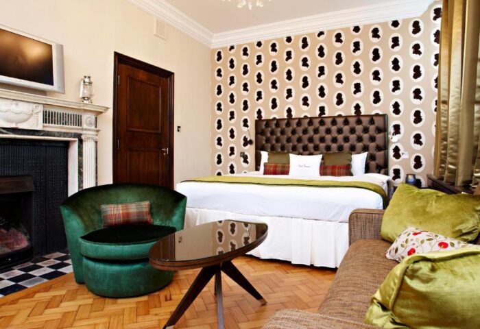 Courthouse Hotel's gay-friendly, pet-friendly room. Features a bed, sofa, chair, fireplace, and unique wallpaper. Ideal for gay travel.