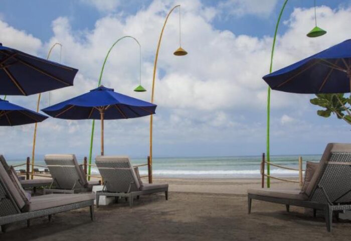 Beachfront at Courtyard Bali Seminyak Resort, a gay-friendly hotel. Relaxing lounge chairs under blue umbrellas. Perfect for Bali holidays.