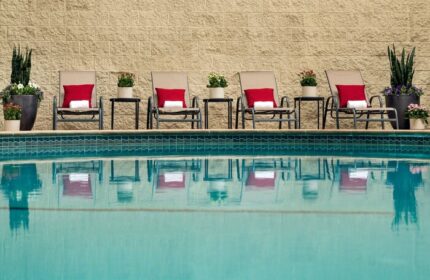 Courtyard Long Beach Downtown pool view. Gay-friendly hotel with chairs, red pillows, side tables, and potted plants. Relaxing travel for gay men.