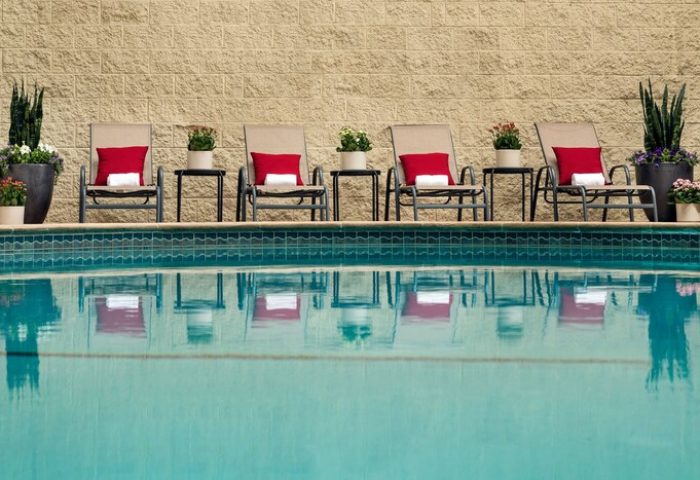 Courtyard Long Beach Downtown pool view. Gay-friendly hotel with chairs, red pillows, side tables, and potted plants. Relaxing travel for gay men.