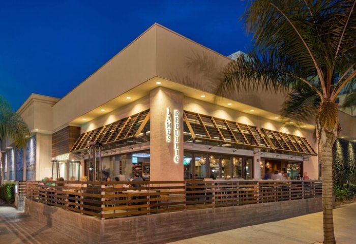 Courtyard Long Beach Downtown gay-friendly hotel. Outdoor dining at James Republic restaurant. Palm tree, modern architecture, and warm lighting.