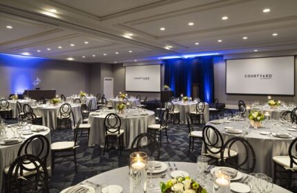 Courtyard Long Beach Downtown gay-friendly hotel ballroom. Round tables set for a wedding or event. Courtyard by Marriott logo on screens.