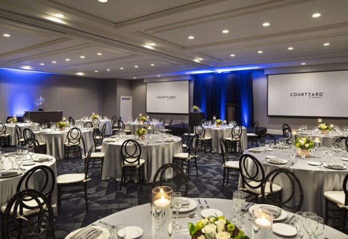 Courtyard Long Beach Downtown gay-friendly hotel ballroom. Round tables set for a wedding or event. Courtyard by Marriott logo on screens.
