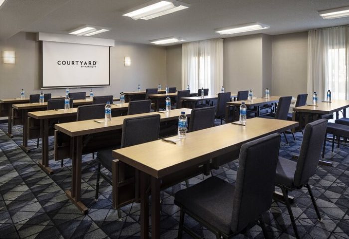Courtyard Palm Springs gay-friendly hotel meeting room. Tables and chairs are neatly arranged, ready for a conference or event. Projector screen visible.