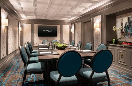 Courtyard San Francisco Downtown/Van Ness Ave meeting room. Boardroom table with blue chairs, TV screen, and modern decor. Gay-friendly hotel.