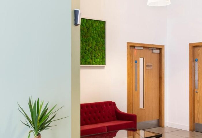 Cove Minshull Street's stylish lobby. A gay-friendly hotel with modern decor, featuring a red sofa, plant, and moss art. Ideal for gay travel.