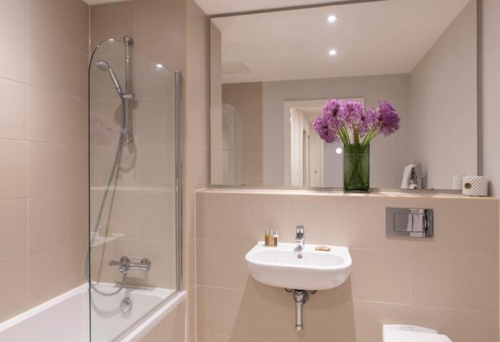 Bathroom at Cove Minshull Street, a gay-friendly hotel. Bathtub with shower, sink, mirror, and purple flowers. Modern design for gay travelers.