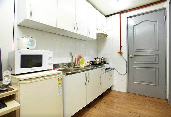 Kitchen at CozyPlace Guesthouse in Itaewon, a gay-friendly hotel. Features white cabinets, microwave, fridge, sink, and stove. Ideal for gay travelers.