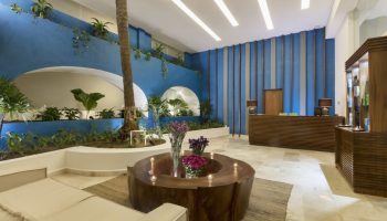 Crown Paradise Golden All Inclusive Adults Only gay-friendly hotel lobby. Modern design with blue walls, plants, and unique wood furniture.