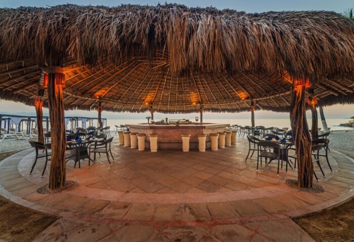 Crown Paradise Golden All Inclusive Adults Only gay-friendly hotel beach bar. Thatched roof, stools, tables, and chairs on the sand.
