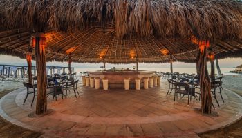 Crown Paradise Golden All Inclusive Adults Only gay-friendly hotel beach bar. Thatched roof, stools, tables, and chairs on the sand.