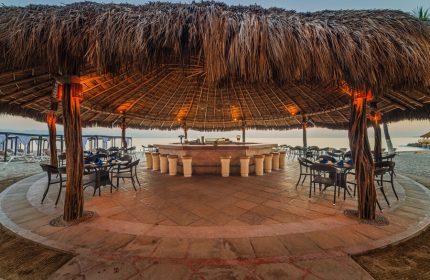 Crown Paradise Golden All Inclusive Adults Only gay-friendly hotel beach bar. Thatched roof, stools, tables, and chairs on the sand.