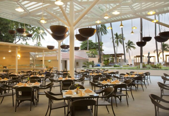 Crown Paradise Golden All Inclusive Adults Only gay-friendly hotel restaurant. Tables set for dining, palm trees in background.