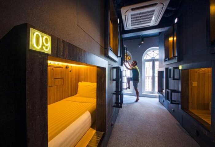 Cube Boutique Capsule Hotel @ Chinatown interior. Gay-friendly hotel room with pod beds. Man climbing ladder to top bunk. Chinatown lodging.