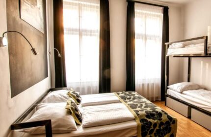 Czech Inn, gay-friendly hotel room. Double bed with floral runner, bunk beds, black curtains, and modern lamps. Ideal for gay travel.