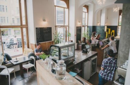 Czech Inn's cafe, a gay-friendly hotel in Prague. Interior view of the cafe, showing customers at tables and the counter. Airy, modern design.