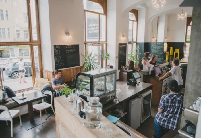 Czech Inn's cafe, a gay-friendly hotel in Prague. Interior view of the cafe, showing customers at tables and the counter. Airy, modern design.