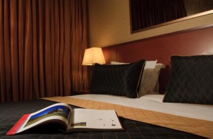 Dan Tel Aviv Hotel guest room. Gay-friendly hotel with a bed, pillows, lamp, and open book. Stylish, comfortable accommodations.
