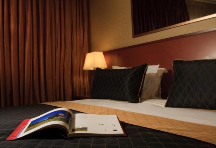 Dan Tel Aviv Hotel guest room. Gay-friendly hotel with a bed, pillows, lamp, and open book. Stylish, comfortable accommodations.