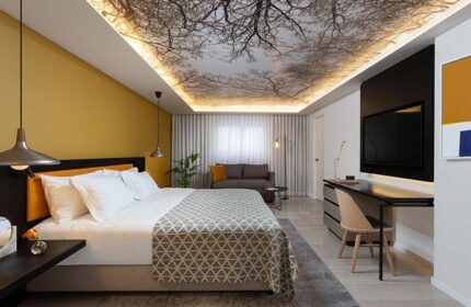 Dan Tel Aviv Hotel gay-friendly room. Modern design with tree branch ceiling art. Comfortable bed, seating area, and workspace.