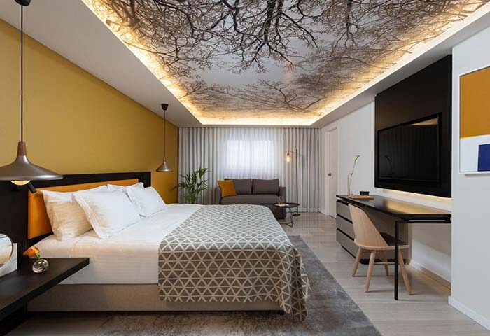 Dan Tel Aviv Hotel gay-friendly room. Modern design with tree branch ceiling art. Comfortable bed, seating area, and workspace.
