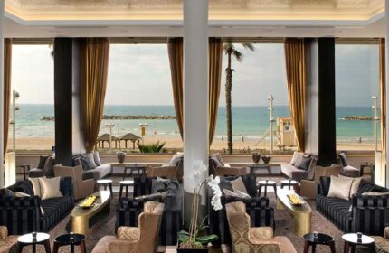 Dan Tel Aviv Hotel's gay-friendly lounge area with ocean view. Beach, palm trees, and stylish seating. Perfect for gay travelers.