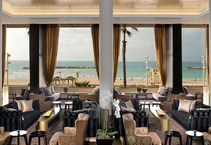 Dan Tel Aviv Hotel's gay-friendly lounge area with ocean view. Beach, palm trees, and stylish seating. Perfect for gay travelers.