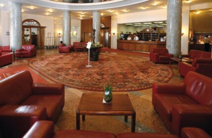 Danubius Hotel Gellert's lobby. Round reception desk, red leather seating, & patterned carpet. Gay-friendly hotel for gay travelers.