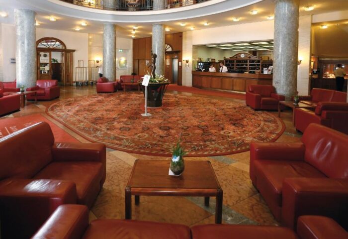 Danubius Hotel Gellert's lobby. Round reception desk, red leather seating, & patterned carpet. Gay-friendly hotel for gay travelers.
