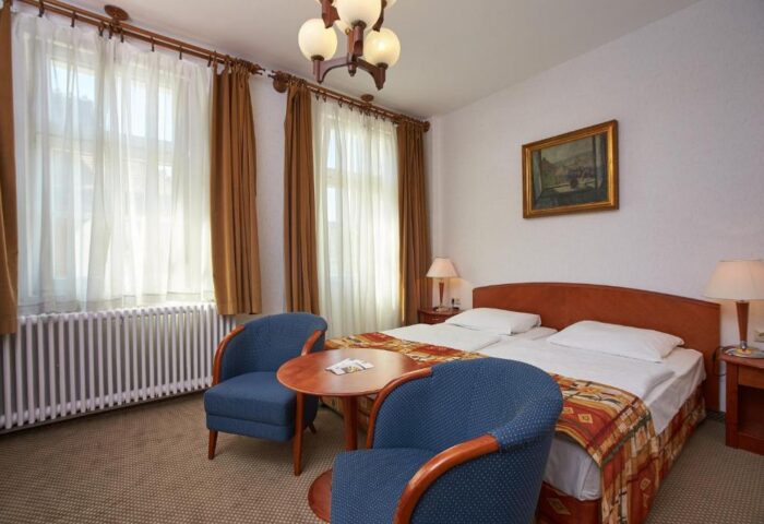 Danubius Hotel Gellert room. Gay-friendly hotel bedroom with twin beds, blue chairs, and a round table. Comfortable stay for gay travelers.