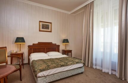 Danubius Hotel Gellert room. Gay-friendly hotel with double bed, nightstands, lamps, curtains, and a chair. Budapest travel for gay men.