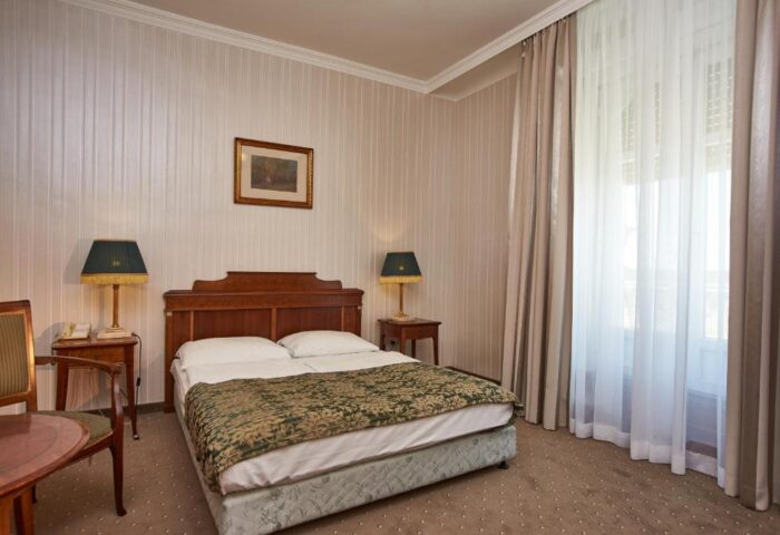 Danubius Hotel Gellert room. Gay-friendly hotel with double bed, nightstands, lamps, curtains, and a chair. Budapest travel for gay men.