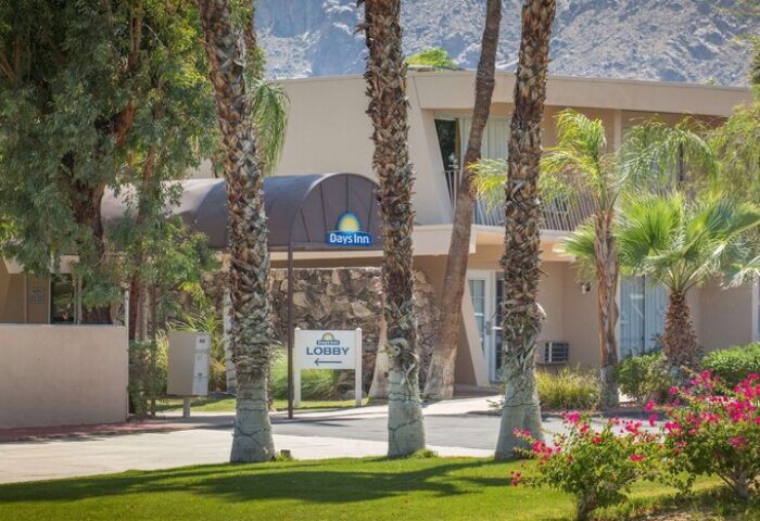 Days Inn by Wyndham Palm Springs exterior. Gay-friendly hotel with mountain views, palm trees, and lobby entrance. Ideal for gay travel.
