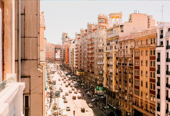 View from Dear Hotel Madrid, a gay-friendly hotel. A bustling Madrid street scene with cars, buildings, and people. Gay travel advice.
