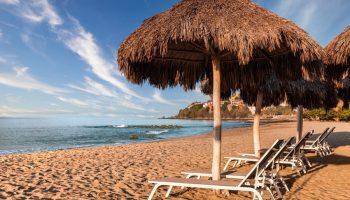 Beach at Delta Hotels by Marriott Riviera Nayarit All-Inclusive. Thatched umbrellas shade lounge chairs on the sand. Gay-friendly hotel.