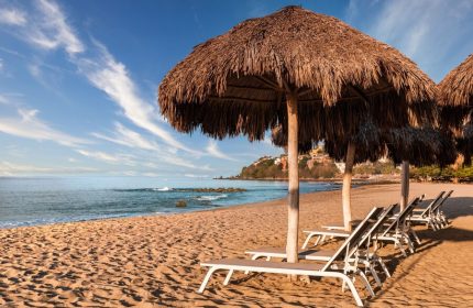 Beach at Delta Hotels by Marriott Riviera Nayarit All-Inclusive. Thatched umbrellas shade lounge chairs on the sand. Gay-friendly hotel.