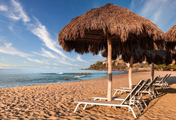 Beach at Delta Hotels by Marriott Riviera Nayarit All-Inclusive. Thatched umbrellas shade lounge chairs on the sand. Gay-friendly hotel.