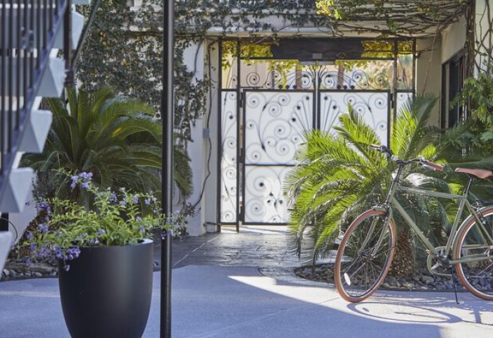 Descanso Resort, a men's resort. Gay-friendly hotel entrance with bike, plants, and decorative gate. Relaxing Palm Springs destination.