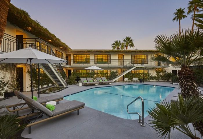 Descanso Resort, a gay-friendly men's resort. Pool view at dusk, lounge chairs, palm trees, and two-story building with exterior staircases.