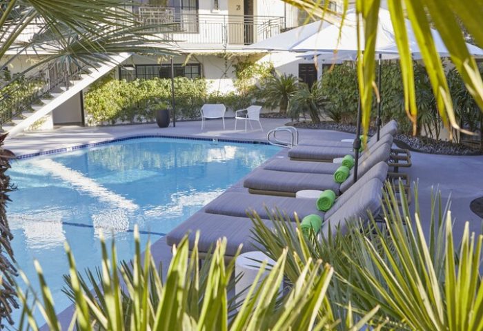 Descanso Resort pool scene. Gay-friendly hotel with lounge chairs, umbrellas, and lush greenery. A relaxing men's resort destination.