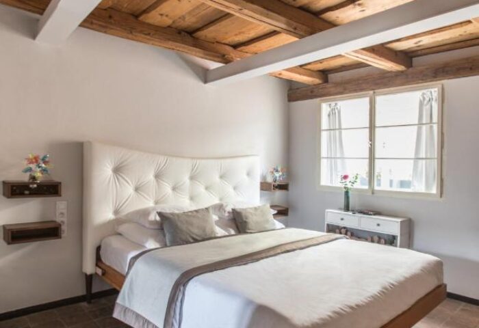 Design Hotel Neruda bedroom. Gay-friendly hotel room with a white bed, wood ceiling, and brick floor. A modern, stylish space for gay travelers.