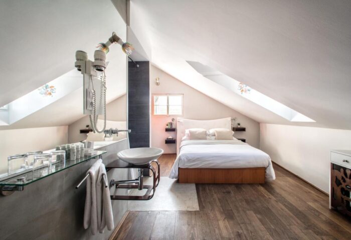Design Hotel Neruda gay-friendly room. Attic bedroom with wood floor, white walls, bed, and sink. Modern design for gay men travelers.